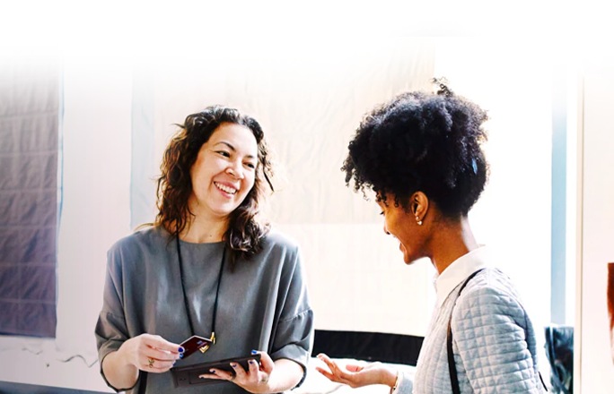 Duas mulheres estão interagindo, uma está sorrindo com um cartão de crédito na mão enquanto a outra sorri.