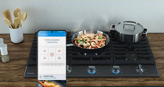 uma tela de celular em primeiro plano e atrás um cooktop com pratos de comida
