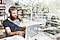 Uma foto com exposição dupla de um homem sentado à mesa com seu computador portátil; há uma estante no fundo