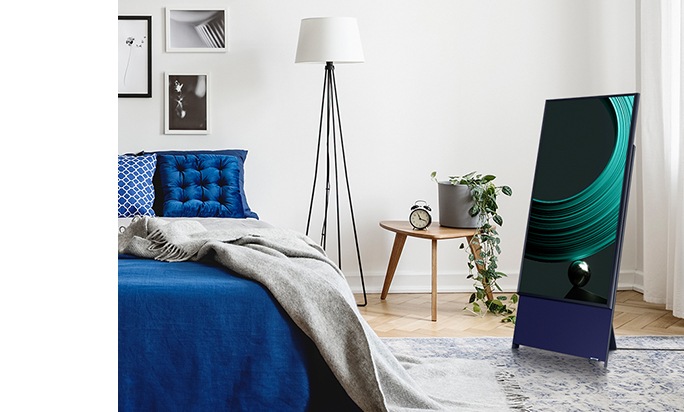 Dentro de um quarto, a TV The Sero é vista em pé na posição vertical, ao lado da cama, sem precisar de um suporte de parede ou suporte adicional. Uma imagem colorida com design e formato artístico pode ser vista na tela.