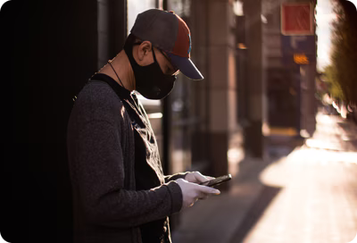 A masked man uses his Galaxy phone on a city street.