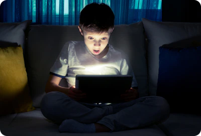 A child illuminated by the screen of a Samsung Galaxy tablet in a dark room.