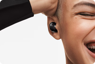 A smiling young adult is wearing Samsung Galaxy Buds.