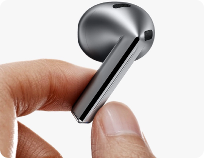 Someone is holding a Galaxy Buds3 earbud by the stem to clean the touch area.