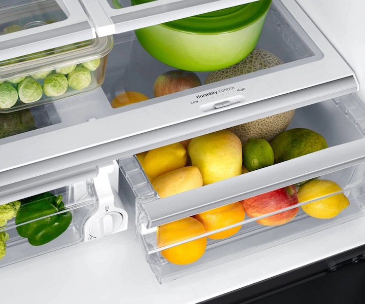 Inside view of a full Samsung refrigerator, highlighting a vegetable crisper drawer with a humidity control slider, packed with vegetables and a container