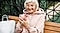 An older woman wearing a pink sweater sits on a bench, using a pink Samsung Galaxy S21 phone.