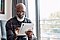 An older man with glasses is sitting down in front of a window with a silver Galaxy Tab S7 in his hands.