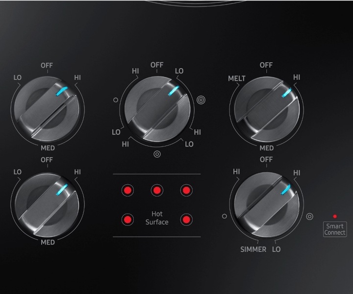 Panneau de commande d’une plaque de cuisson Samsung avec des boutons de commande métalliques et des voyants de surface chaude allumés.