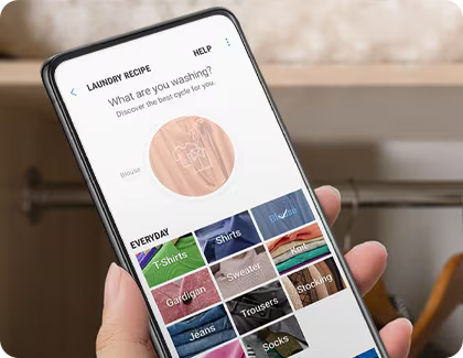 A hand holding a phone displaying the SmartThings app, which offers various laundry options to help select the optimal washing settings.