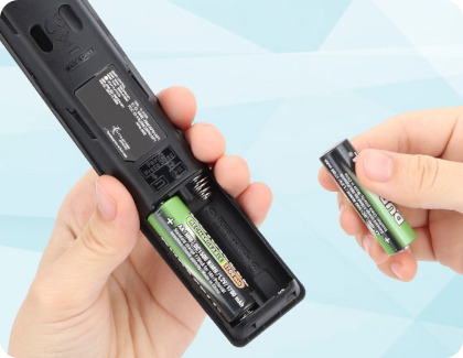 Hands replacing batteries in a Samsung TV remote control, inserting a new AA battery into the compartment.