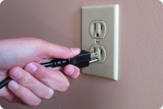 A hand unplugging a power cord from a wall outlet.