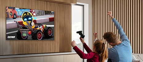 A child and a parent are joyfully engaged in a game on TV, with three KartRider characters displayed on the screen.