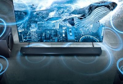 Téléviseur Samsung présentant un paysage urbain holographique et l'affichage d'une baleine, avec une barre de son en dessous, mettant en avant une technologie avancée de divertissement à domicile.