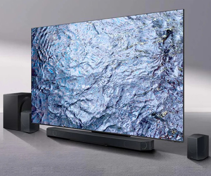 Un téléviseur Samsung affichant une image abstraite en haute définition, accompagné d'une barre de son et de deux enceintes sans fil disposées de chaque côté.