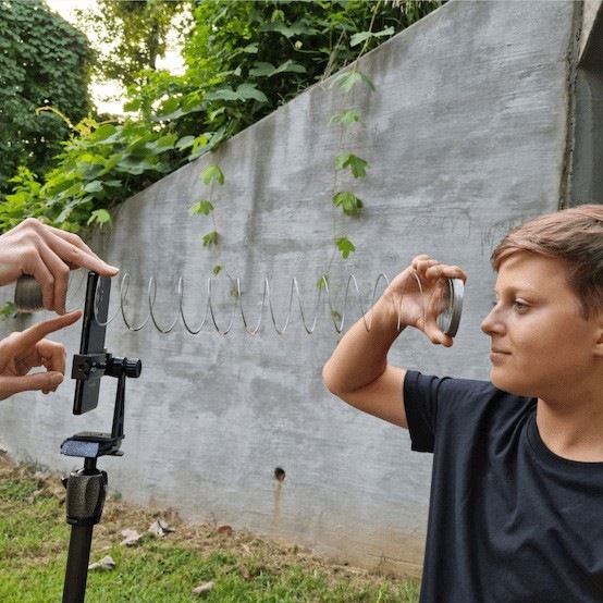 Une vue dans les coulisses d’un garçon photographié à travers un slinky avec le Galaxy S21 Ultra 5G. Il tient une extrémité du slinky sur son visage, tandis que le photographe tient l’autre extrémité à l’objectif de l’appareil photo.