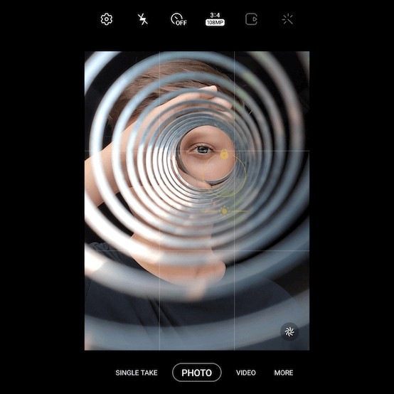 Gros plan de l’œil d’un garçon photographié à travers les spirales d’un slinky argenté.