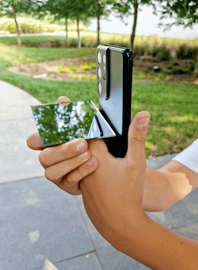 Des mains tenant un petit miroir contre un Galaxy S21 Ultra 5G noir fantôme juste en dessous de l’objectif de l’appareil photo