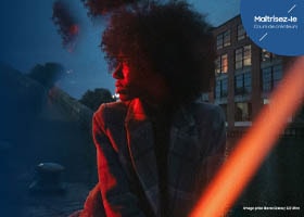 Une femme portant une veste regardant vers la gauche, subtilement illuminée par une lumière rouge devant un ciel bleu.  Master it. Creator classes.