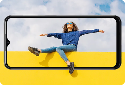 Une jeune femme portant un chandail bleu et des lunettes de soleil étend joyeusement les bras et les jambes, en flottant sur un fond jaune vif, affichée sur l’écran d’un téléphone Samsung Galaxy.
