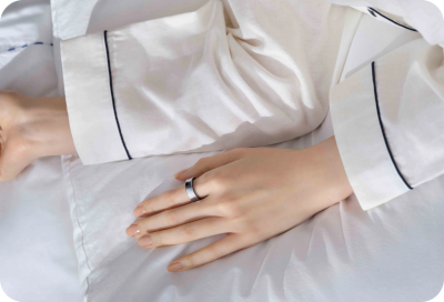 Gros plan sur la main d'une personne portant une Galaxy Ring tout en se reposant sur un lit, mettant en évidence la fonction de suivi du sommeil.