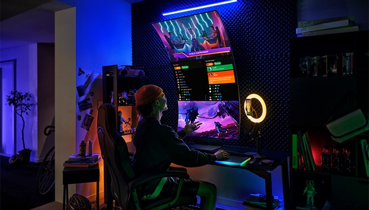 Ein Gamer sitzt in einem futuristischen Raum mit blauer Beleuchtung an einem grossen Curved-Monitor. Im Hintergrund sind Regale und Dekor.