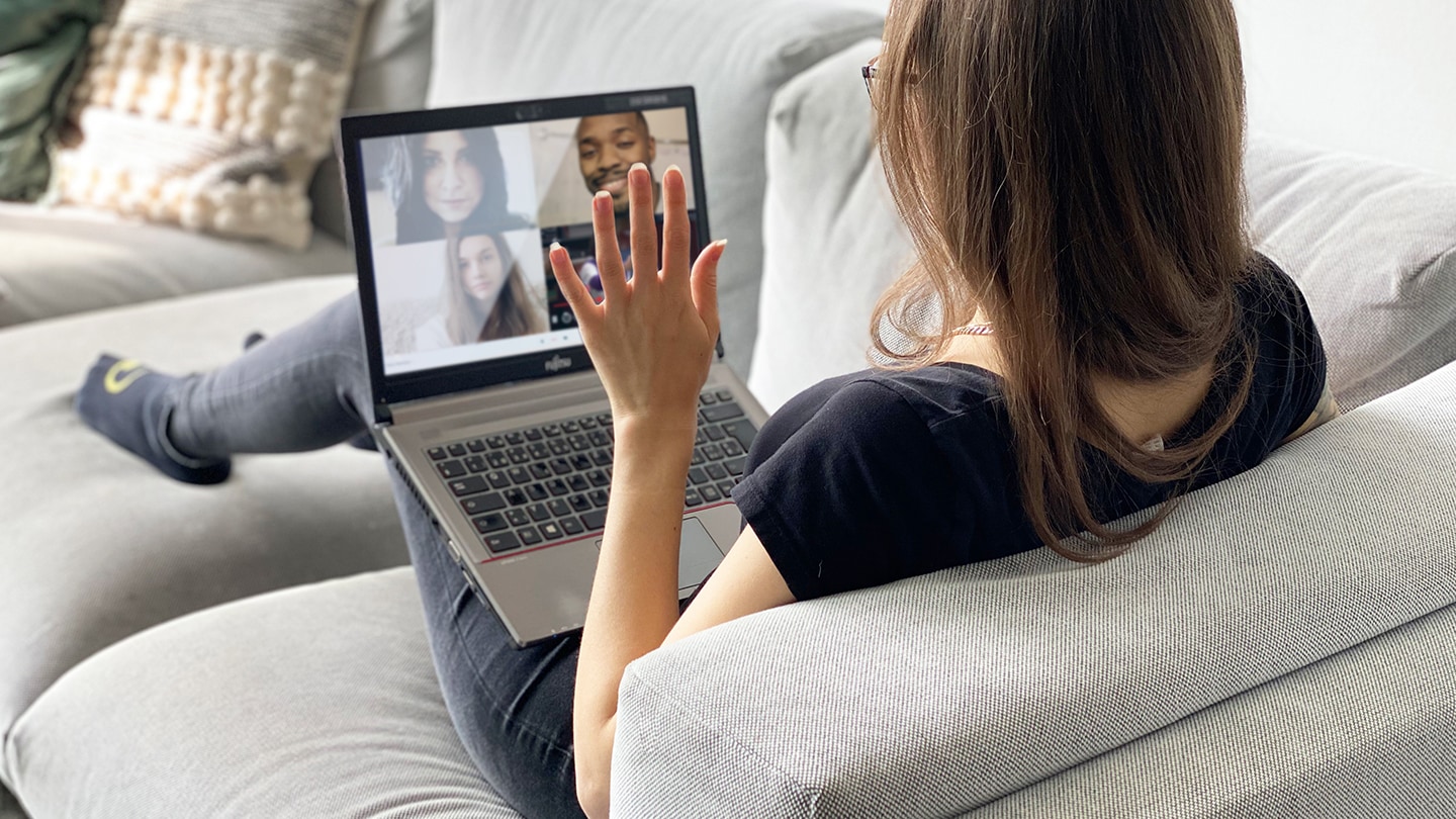 Frau sitzt mit kleinem Mädchen auf dem Schoss auf einem grünen Sofa und winkt in einen Screen