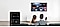 Ein Paar sitzt auf einer Couch und schaut auf den an der Wand befestigten Fernseher, wobei der Mann ein Smartphone als Fernbedienung nutzt. Der TV-Bildschirm zeigt eine Auswahl von Streaming-Apps und Sendungen an. Eine Nahaufnahme des Smartphone-Bildschirms zeigt die Bedienoberfläche der TV-Fernbedienung.