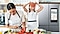 Une mère coupant un poivron dans la cuisine tandis que sa fille en tient deux rondelles devant ses yeux, avec un réfrigérateur Samsung Family Hub™ en arrière-plan.