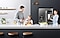 Ein Vater und eine Tochter bereiten Eier und Orangensaft auf der Küchentheke zu, während die Mutter über sie wacht und lächelt, während sie neben dem Family Hub mit dem Bildschirm im On-Modus steht.