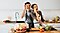 Jeune couple tenant des tranches de poivron devant leurs yeux et s’amusant pendant qu’ils préparent à manger dans la cuisine.