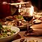 Photo de plats gastronomiques posés sur une table éclairée à la bougie, avec une main tenant le pied d’un verre de vin.