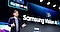 Un hombre está parado en un escenario en frente de una pantalla grande que dice “Samsung Vision AI”. Está hablando, con una mano levantada en un gesto a mitad del discurso.