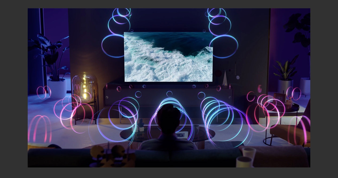 Un hombre disfruta en su sala de estar de las imágenes y del audio del océano en el televisor con la barra de sonido. Las ondas de audio se proyectan desde los altavoces superiores del televisor y la barra de sonido.