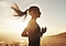 Una mujer que corre con un amanecer de fondo. Su cabello se mueve con el viento para mostrar el movimiento dinámico.