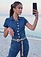 Una mujer con un mono vaquero se toma una selfie en una playa con arena.
