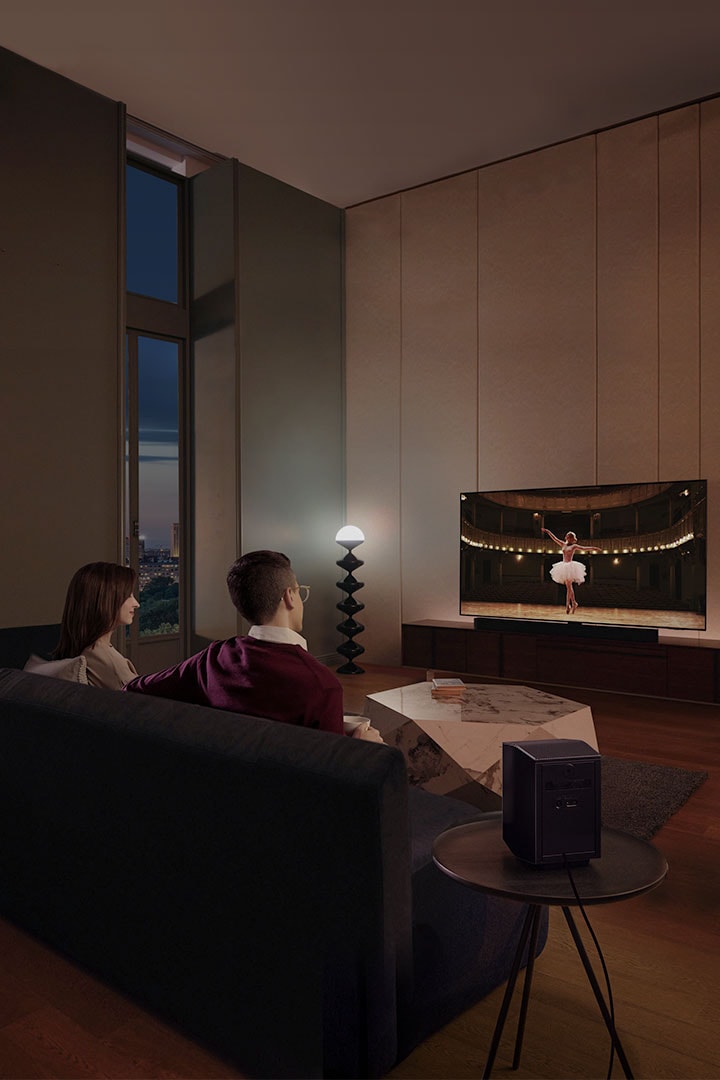 Una pareja disfruta de una noche de película en su sala con el sonido surround tipo cine de la Barra de sonido Samsung.