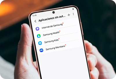 Una mano sujetando un teléfono galaxy con el menú de aplicaciones en segundo plano en pantalla