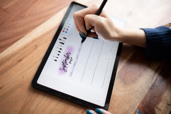 Toma desde arriba de una Galaxy Tab S6 Lite negra un poco inclinada hacia la izquierda. La mano derecha de Amanda está escribiendo con un S Pen negro. En la pantalla, aparece una lista semanal de septiembre de 2020, creada con la aplicación Samsung Notes.