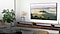 Un televisor de pantalla grande montado en la pared que muestra un paisaje campestre en una sala de estar iluminada por el sol.