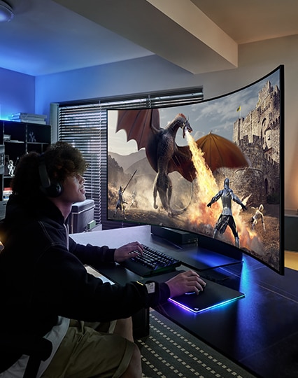 Um homem está jogando com um monitor. Há um dragão e algumas pessoas na cena do jogo.