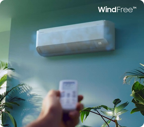 Ruka s dálkovým ovladačem namíří na klimatizaci Samsung Windfree. Stisknutím tlačítka se uzavře ventilátor a z klimatizace začne vycházet bílá mlha, která znázorňuje chlazení.