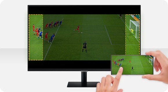 Uživatel hrající hru na chytrém telefonu, která je zobrazována na větším displeji monitoru, nacházejícím se za ním.