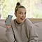 Millie Bobby Brown sedí na gauči a drží Galaxy Note10 v provedení Aura Glow