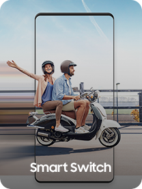 Muž jede na skútru po městě a žena sedící za ním se natahuje směrem ke kameře. Oba mají na hlavě helmy.