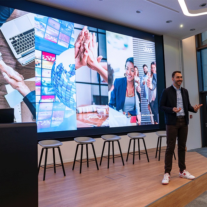 Ein Mann steht auf einer Bühne, hinter ihm ein Samsung the Wall an der Wand, auf dem eine Präsentation zu sehen ist.