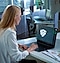 In einem modern eingerichteten Büro sitzt eine Frau, die eine Brille trägt, an ihrem Schreibtisch und schaut auf ihr Galaxy Book, auf dessen Bildschirm ein großes Samsung Knox Vault-Logo zu sehen ist.