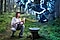 Junge Frau kniet im Wald mit ihrem Galaxy S24Ultra in der Hand und fotografiert den Donnervogel auf dem Trail "Mystic Valley" in der AR-App Trails of Wonder.