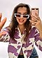 Eine Frau mit einer weißen Sonnenbrille und einer Jacke mit weißem und purpurfarbenem Kuh-Muster nimmt ein Selfie mit einem Spiegel auf.