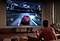Ein Mann spielt auf dem 98-Zoll-Supersize-TV von Samsung, auf dem ein rotes Auto auf dem Bildschirm zu sehen ist, begleitet vom Spielstand und anderen Spielinformationen.