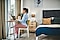 En ung kvinde iført en skjorte med blå krave og flonelpyjamabukser sidder ved sit skrivebord foran sin bærbare computer og skriver. Hun sidder foran et åbent vindue i sit soveværelse.